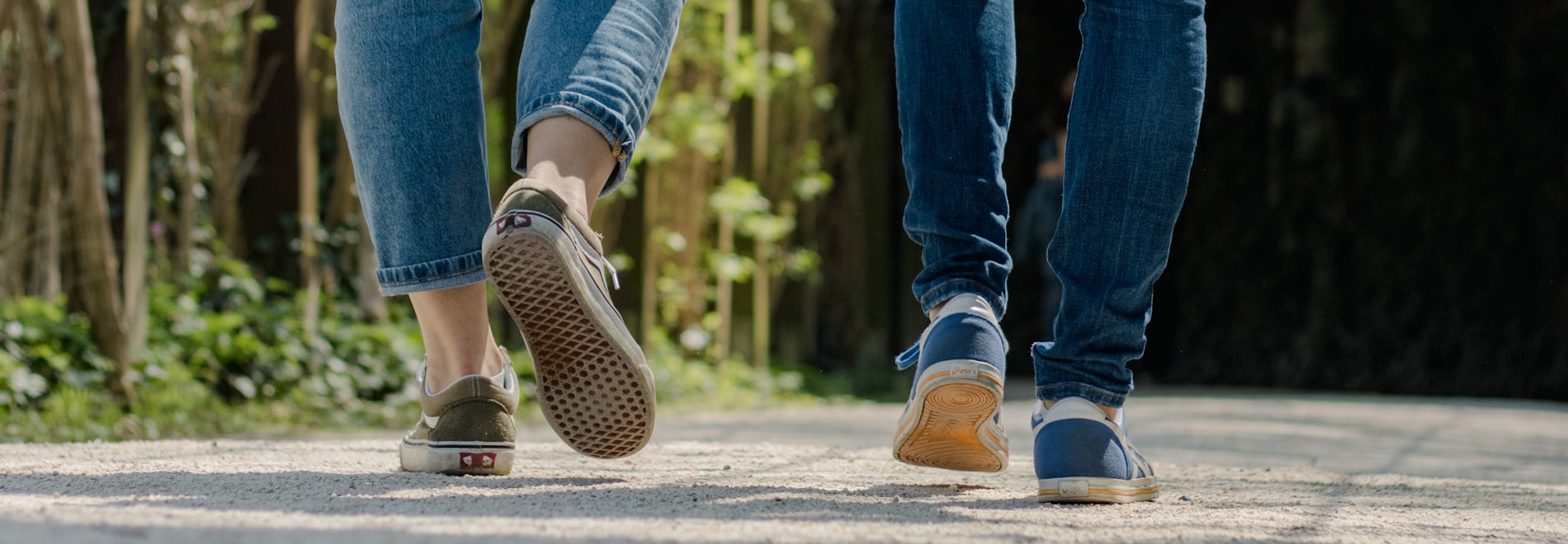 Two people walking away along a sunlit path, seen from the knees down